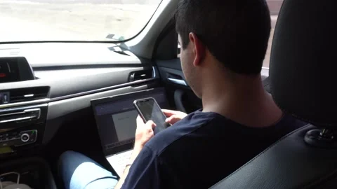 A man working from the car as a co-pilot using his phone and laptop returning Stock Footage 155824818