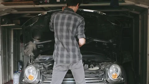 Man working on a car in a garage during the daytime, focusing on repairing the Stock Footage 303809767