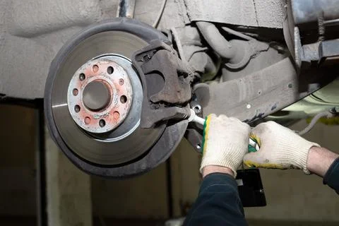 A man working in a car service. Replace brake disc and pads. A young mechanic is Stock Photos