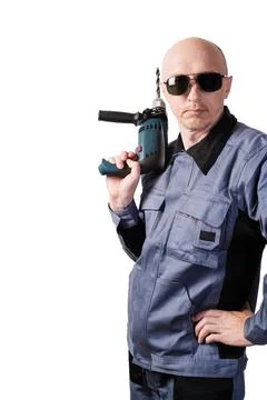 A man in working clothes, in dark protective glasses, with an electric drill Stock Photos