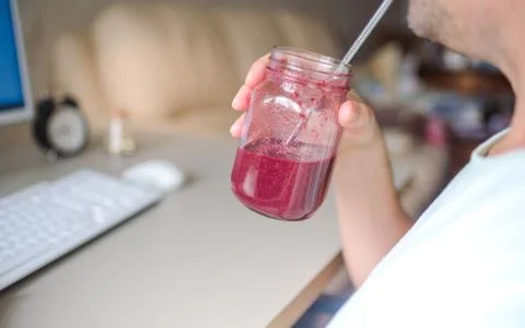 Man working on the computer and drinking smoothie in home office Stock Photos
