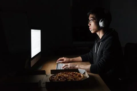 Man working with computer and eating pizza in dark room Stock-Fotos
