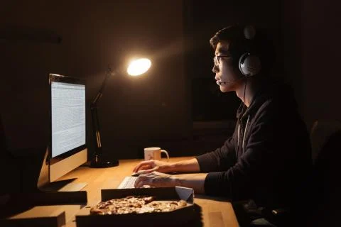 Man working with computer and eating pizza in dark office Stock-Fotos