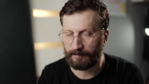 Man working at computer. Bearded man in glasses typing on keyboard and looking a 動画素材 303947955