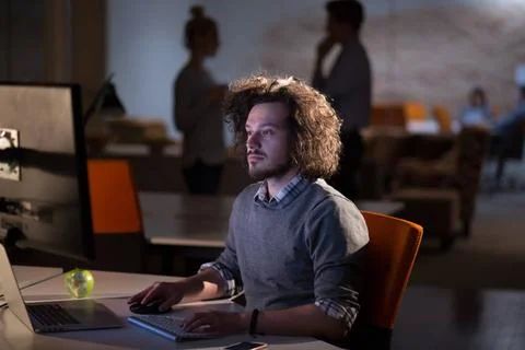 Man working on computer in dark office Young man working on computer at ni... Stock-Fotos