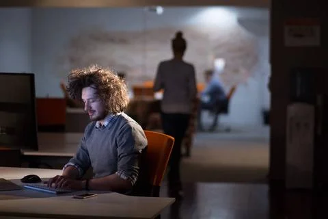 Man working on computer in dark office Young man working on computer at ni... Stock-Fotos