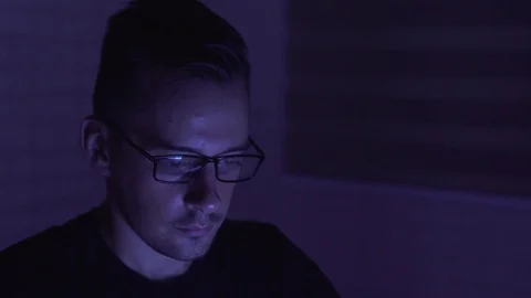 Man working on a computer in darkness, laptop screen reflects on glasses Stock Footage 83191556