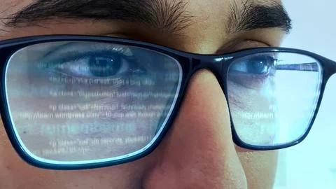 A man working on computer looking at programming code reflecting in his glasses Stock-Fotos