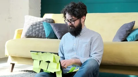 Man working at the computer with a lot of reminder notes, sitting near sofa. Stock Footage 152836888