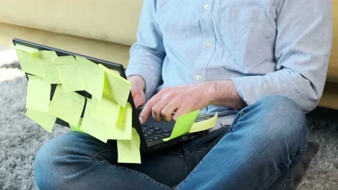 Man working at the computer with a lot of reminder notes, sitting near sofa. Stock Footage 153481915
