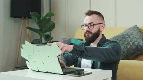 Man working at the computer with a lot of reminder notes, sitting near sofa. Stock Footage 169400102