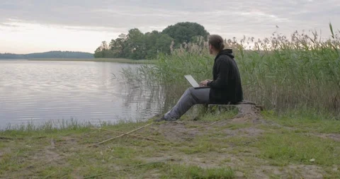 Man working with computer near lake remote work Video stock 243765944