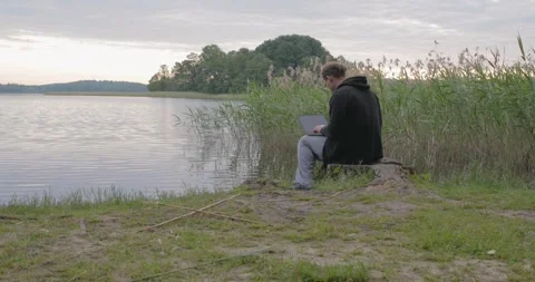 Man working with computer near lake remote work Stockbeeldmateriaal 243765949