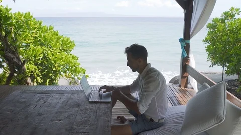 Man working at a computer by the ocean 2 Stock Footage 99586423