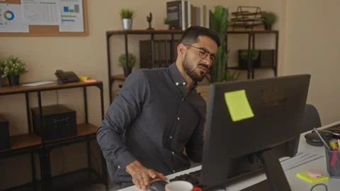 Man working on computer in office, experiencing back pain, surrounded by pl.. Stock Footage 313023261