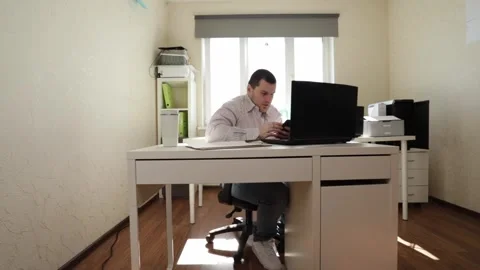 Man Working on Computer with Relaxed Woman Taking Break in Bright Office Stock Footage 309989641