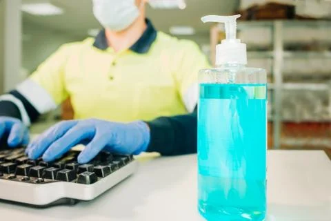 Man working on a computer wearing protective mask, gloves and disinfectant ge Stock Photos
