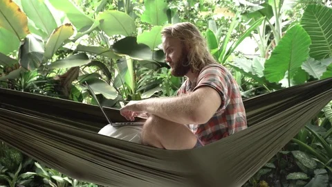 Man working on computer while sitting on hammock Stock Footage 84841302