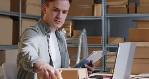 Man working conducts inventory on warehouse cross referencing boxes with Stock Footage 290303148