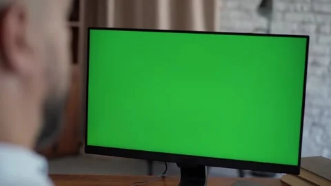 Man Working at Desk Using Computer with Green Mock-up Screen in Cozy Home Office Stock Footage 247461481