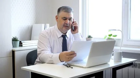 Man Working with Documents and Talking on Phone in Office 库存照片