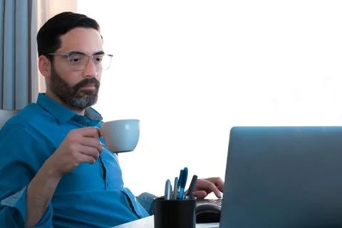 Man working, drinking coffee to keep him awake, cup in hand and typing Stock Photos