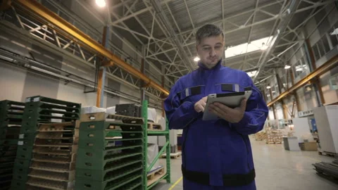 A man is working in a factory with a digital tablet, he is dressed in a blue Stock Footage 91642212