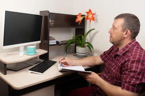 Man working at home at the computer takes notes Stock Photos