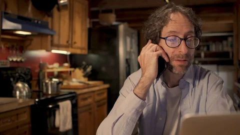 Man working at home in his kitchen talking on his mobile phone Stock-Footage 128177700