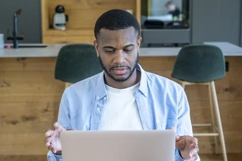 Man working at home kitchen counter looking surprised while using laptop, r.. Foto stock