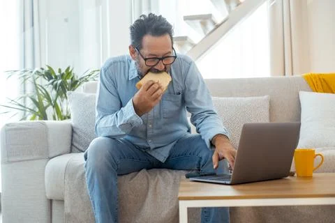 Man working from home on laptop while eating breakfast on the couch with a .. Foto stock