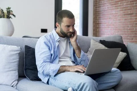 Man working from home on a laptop while sitting on a couch in a modern livi.. Foto stock