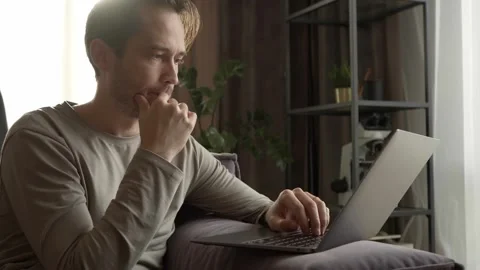 A man is working from home, sitting on the couch and typing on his laptop. Stock Footage 253403306