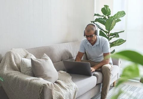 Man working from home sitting on the sofa using laptop and headphones 写真素材
