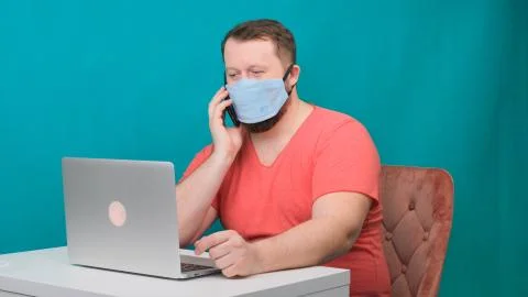 Man working from home. Using a smartphone. Bearded man in a protective mask Stock Photos