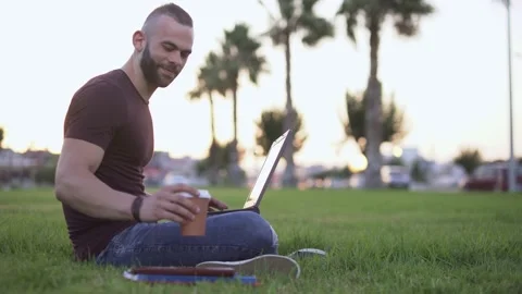 Man working on laptop and drinking coffee in urban park Video stock 136369898