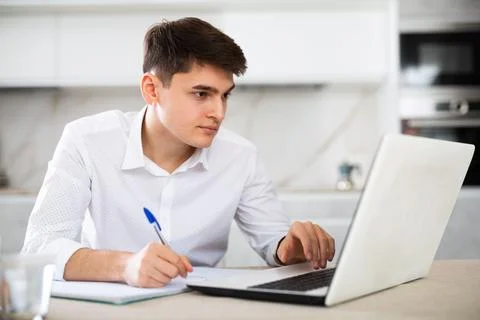 Man working on laptop and making notes in notebook 스톡 사진