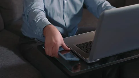 Man working on laptop and picking up phone from table Stock Footage 329945938
