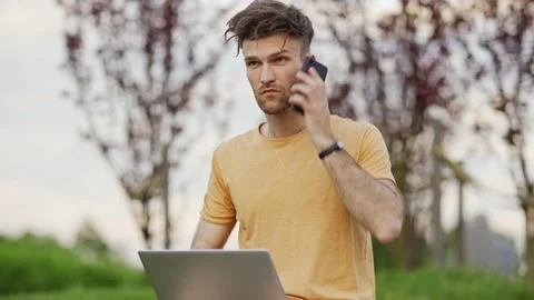 Man working on laptop and talking on phone in park Stock Footage 132728540