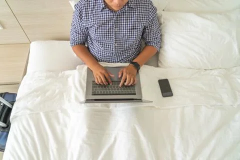 Man working with laptop on bed next to mobile phone Stock Photos