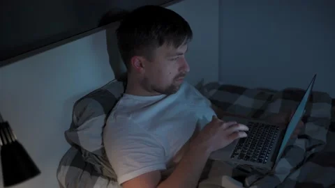 Man working on laptop in bed at night. Guy with insomnia was lying on bed using Stock Footage 145494385