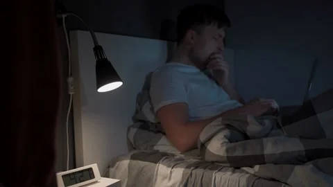 Man working on laptop in bed at night. Guy with insomnia was lying on bed using Stock Footage 145494976