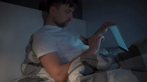 Man working on laptop in bed at night. Guy with insomnia was lying on bed using Stock Footage 145495380