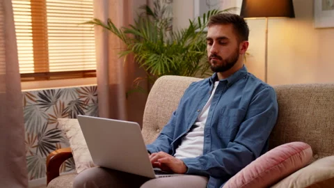 Man Working On Laptop Computer From Home Office Sitting On The Couch Stock Footage 147003187