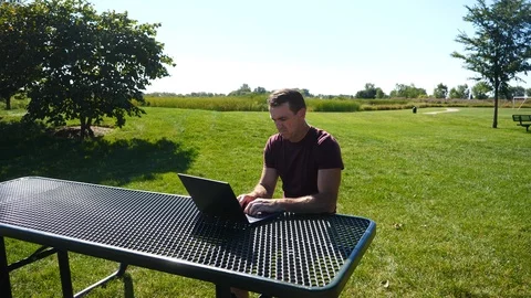 Man working on laptop computer outside at a park on a summer day, 4k, 60fps. Stock Footage 115849366