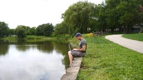 Man working on laptop computer sitting on the water dock 4k, 60fps Stock Footage 115900758