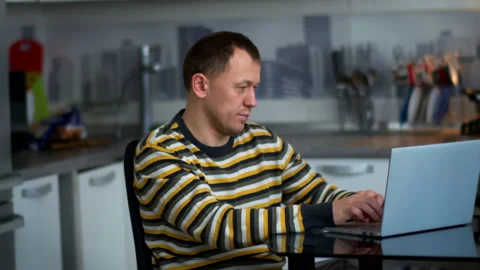 Man working on laptop at home at the table while sitting in the kitchen Stock Footage 132415132