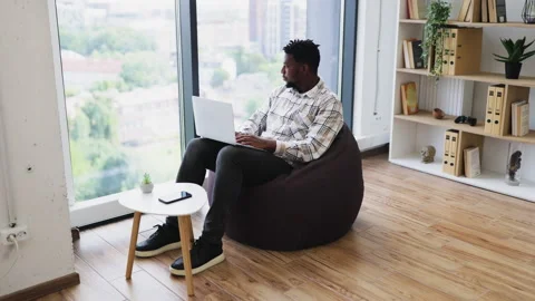 Man working on laptop in modern office with large window and bookshelf Stock Footage 317995037