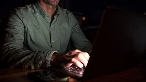 Man working on laptop at night while sitting at a wooden table Stock Photos