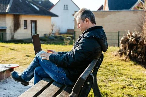 Man working on laptop outdoors, sitting playground. The concept of remote work Stock Photos